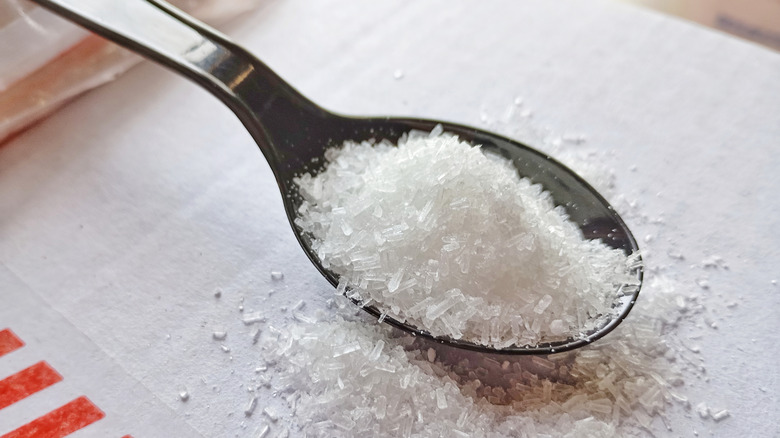 Monosodium glutamate granules on black plastic spoon.