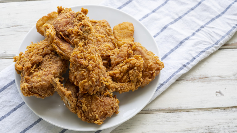 A white plate on a towel with pieces of fried chicken on it.