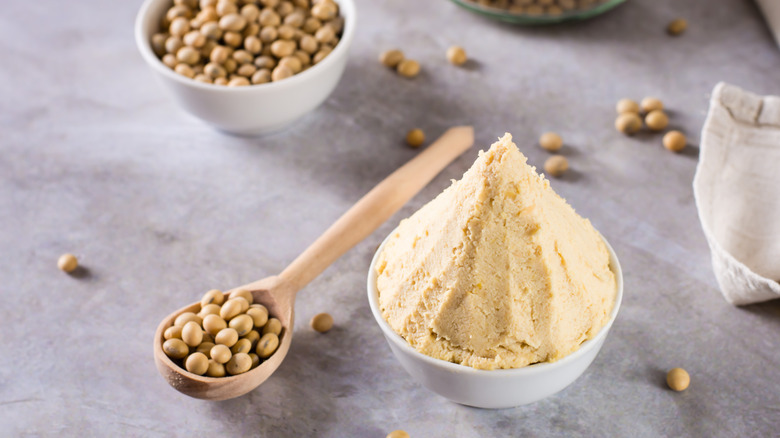 A heaped bowl of white miso paste and a wooden spoon full of soybeans.