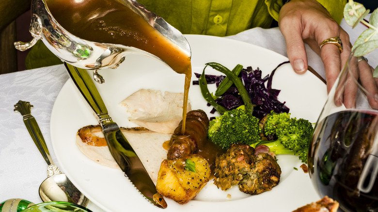 A dinner guest pours gravy over a plate of roasted vegetables
