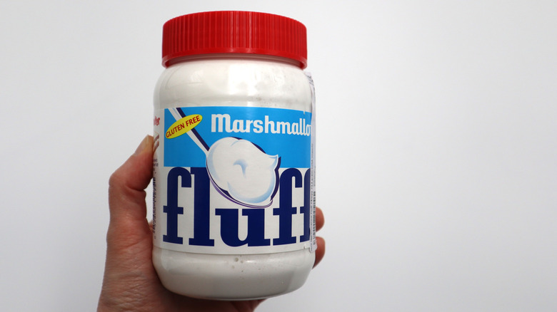 Hand holding a jar of Marshmallow Fluff against a white background