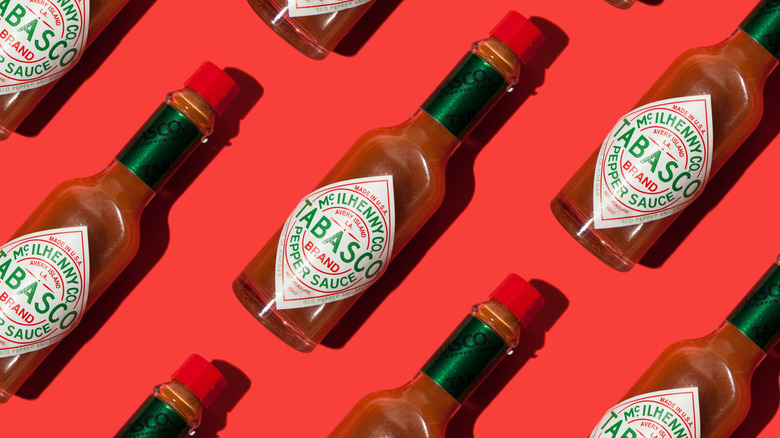 Slanted rows of classic tabasco bottles behind a red background