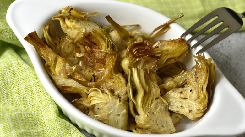 White oval ramekin holding caramelized artichokes with fork near
