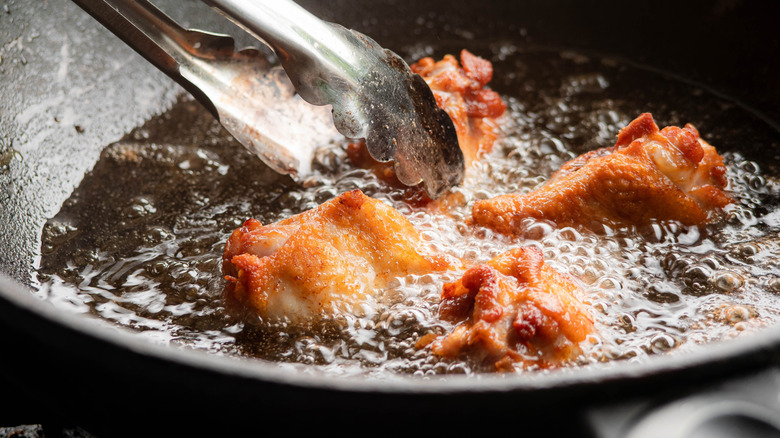 tongs moving frying chicken drumsticks