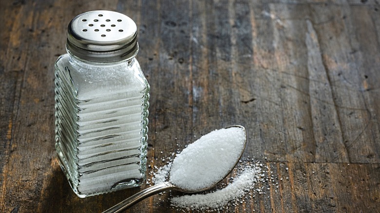 A salt shaker with ridges on the side next to a spoonful of salt