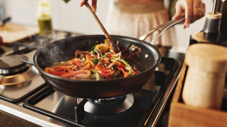 A woman cooks stir-fry vegetables in a pan on a stovetop
