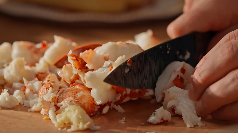 A home cook chops lobster meat on a cutting board