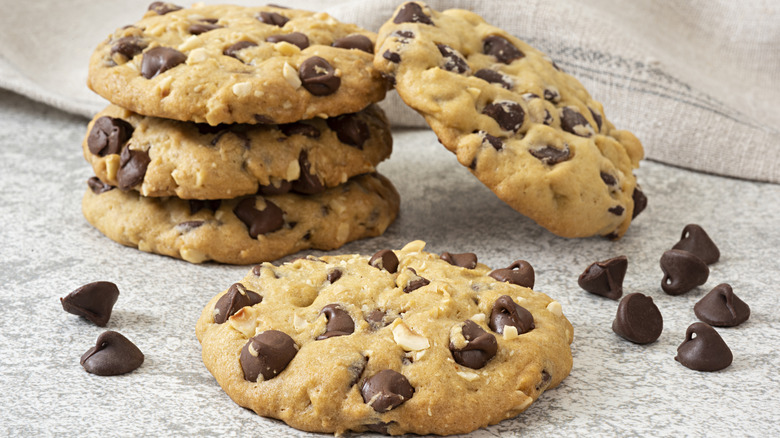 Thick chocolate chip cookies piled on each other with a few chocolate chips nearby