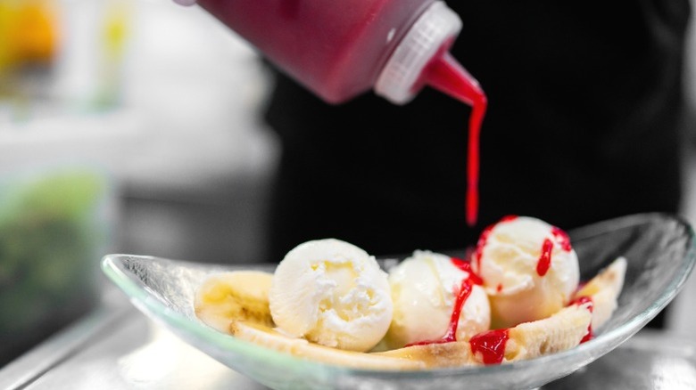 A banana split sundae being prepared in a glass dish.