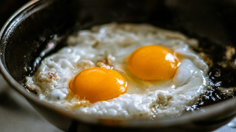 A closeup of two sunnyside-up eggs frying in a pan