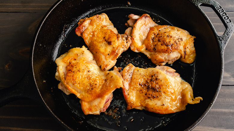 top-down view of four pan-seared chicken thighs in a black pan