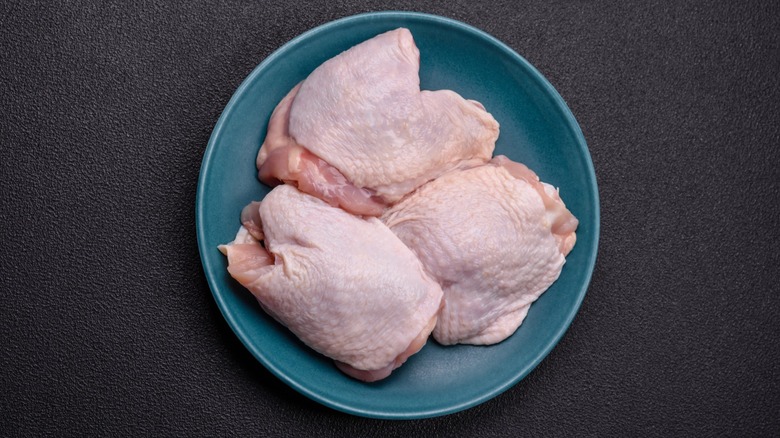 A top-down view of three raw chicken thighs on a blue plate.