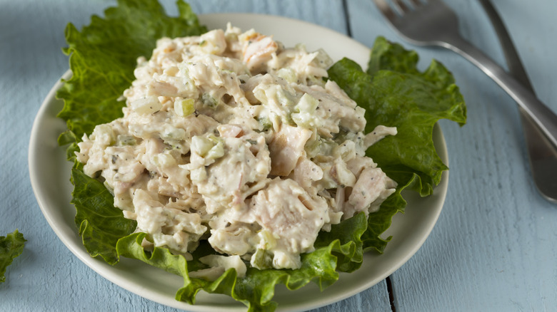 chicken salad piled on a lettuce on a small plate next to a fork