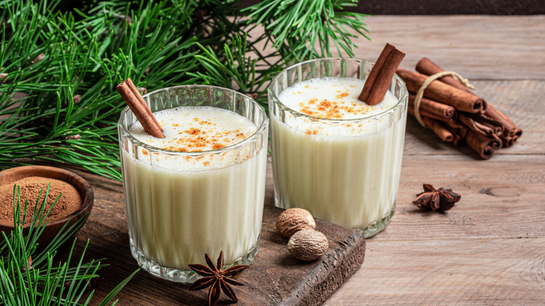 Two glasses of eggnog with cinnamon sticks and cinnamon topping