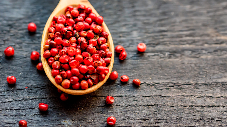 Bright pink peppercorns in a wooden spoon on a black wooden surface
