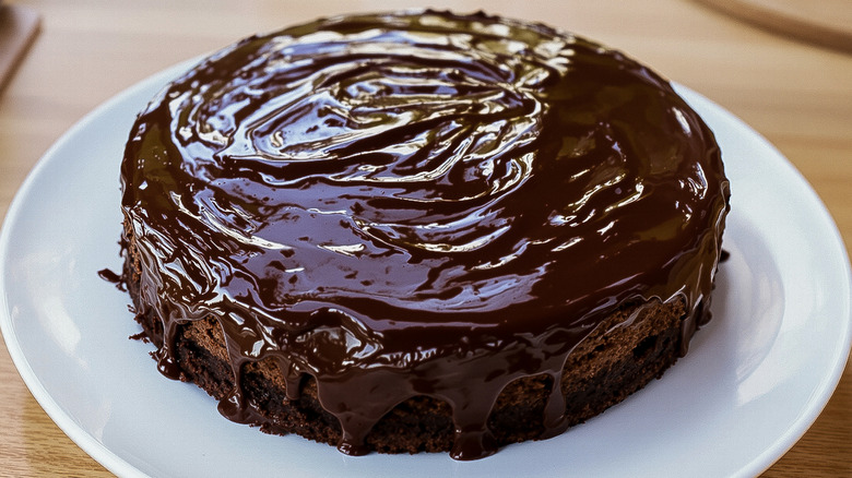 A homemade glazed chocolate cake on a white plate