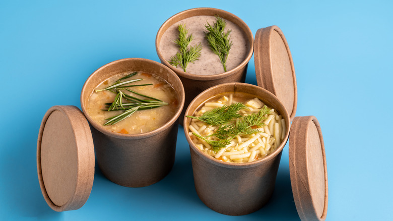 Three soups in takeout containers on a blue background.