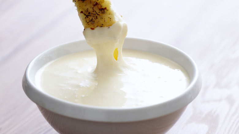 A breadstick being dipped into a thick, white sauce.