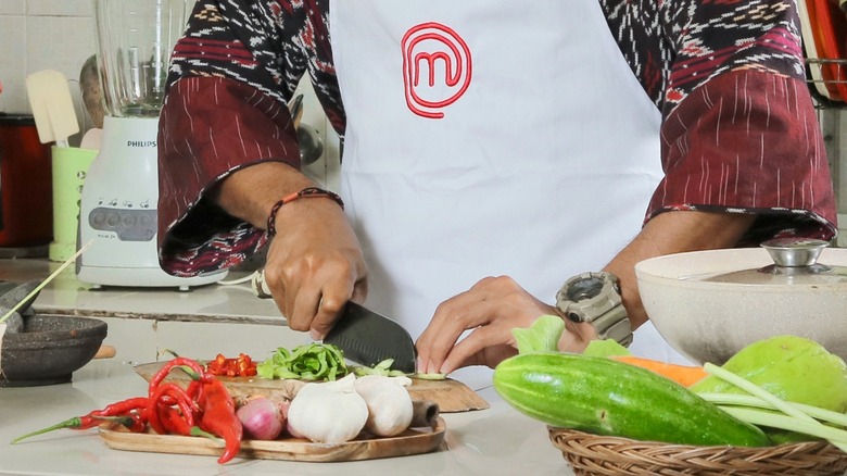 Person wearing MasterChef apron cutting vegetables