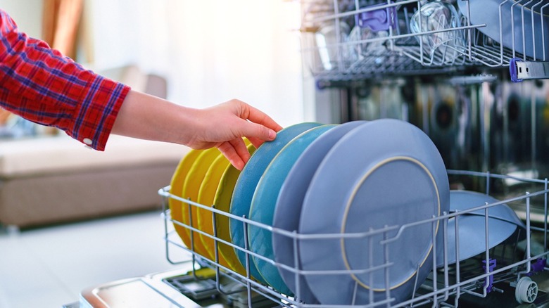 A person loading a modern dishwasher.