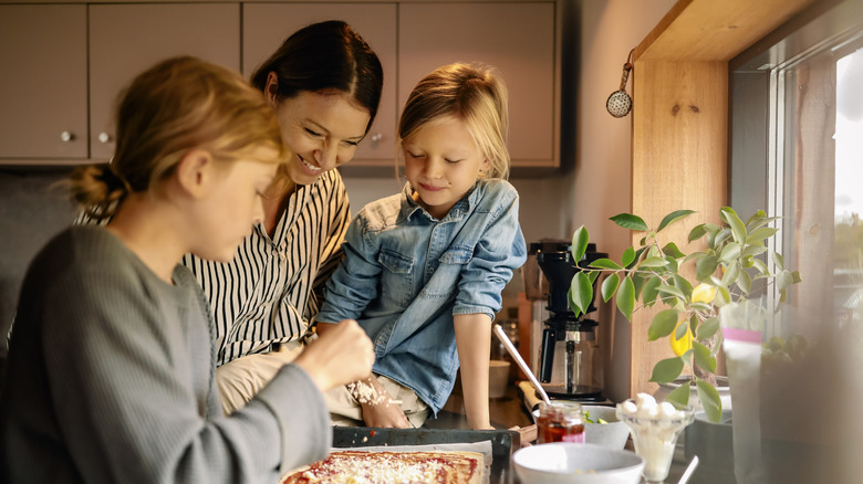 A smiling mother lets her two daughters help in the kitchen