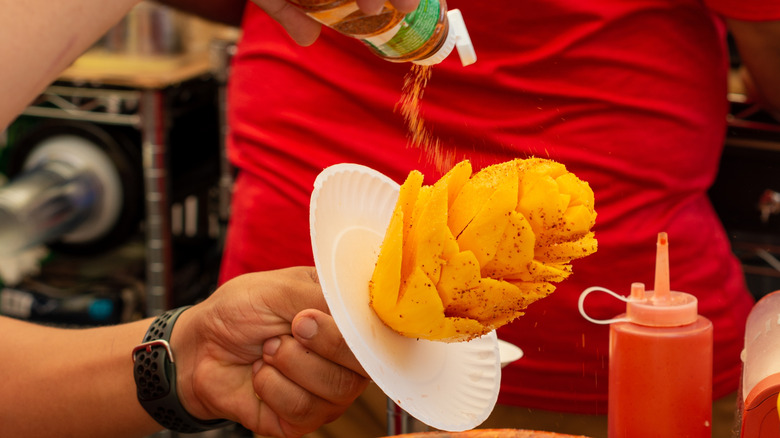 Vendor shakes Tajin seasoning on mango flower