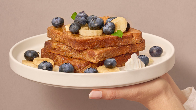 Hands holding plate of French toast with bananas and blueberries