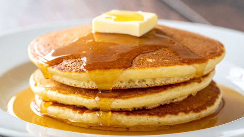 Closeup of three pancakes with butter and syrup on white plate