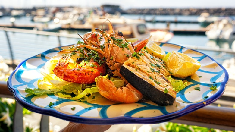 Person serving seafood dish with coastal view in background