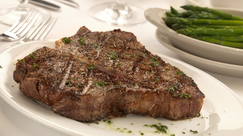 Cooked porterhouse steak on white plate, side of asparagus.