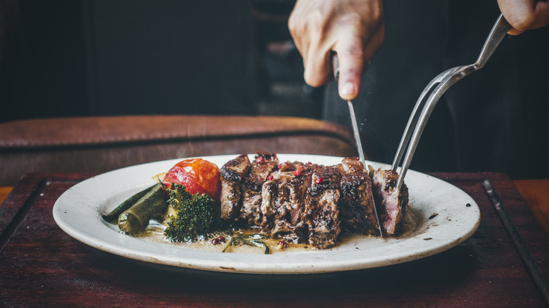 Someone slicing steak on a plate with veggies