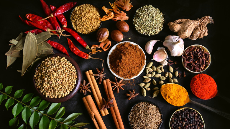 Variety of spices, herbs, and seasonings all on a black table.