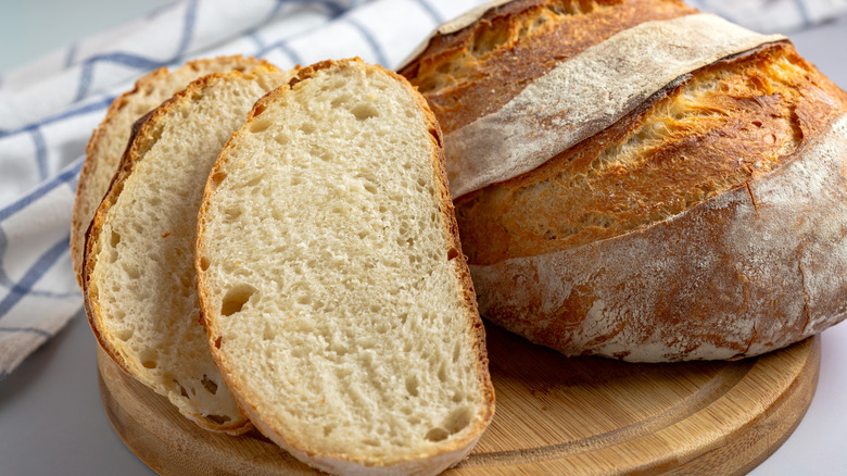 a loaf of Sourdough bread beside three slices of bread on a wooden board.