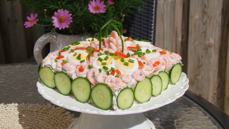 Swedish smörgåstårta decorated with shrimp, boiled eggs, green onions, and cucumber slices