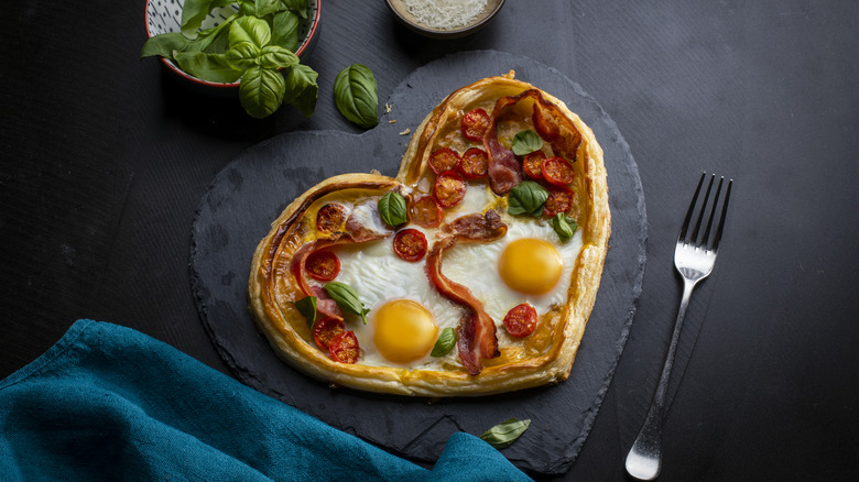 Heart shaped pastry with bacon, eggs, tomatoes on black