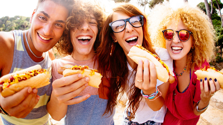 Four people smiling and holding hot dogs
