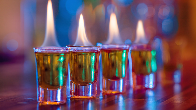 A closeup of a row of flaming shots on a bar