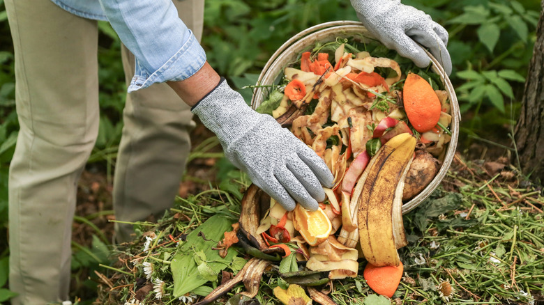 Someone wearing gloves in their backyard and composting vegetable peelings