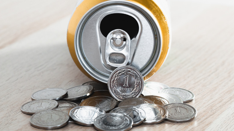 An open aluminum can on its side with various silver coins in front of it