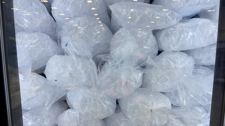 Stacked bags of ice inside a freezer with glass door.