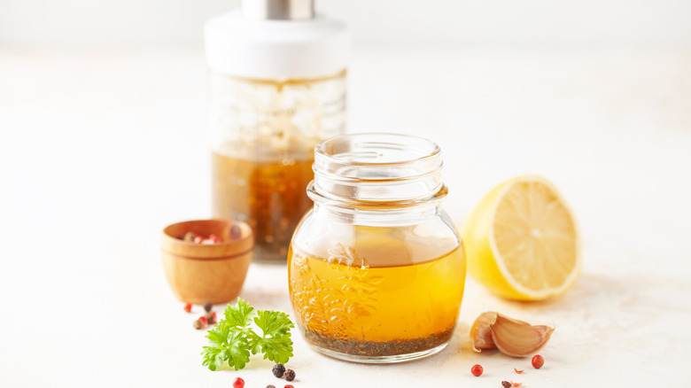 Glass jar with vinaigrette contents in it -- lemon, oil, seasoning and herbs -- with the whole versions of these contents near