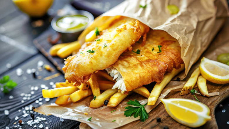 Breaded fish filet in paper underneath fries near lemon wedges