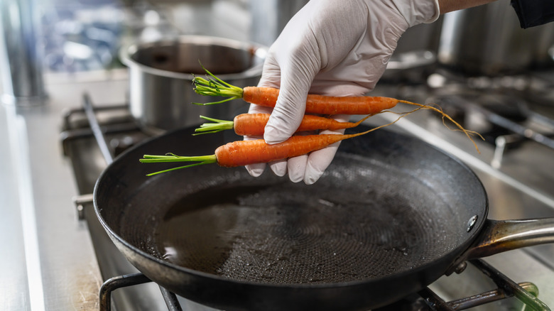 Gloved hand placing raw carrots into oiled frying pan