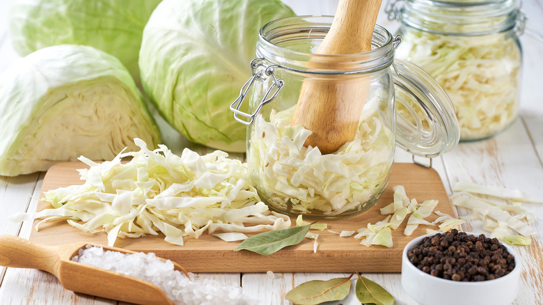 Sliced green cabbage being packed into sealable glass jar with green cabbage heads in the background