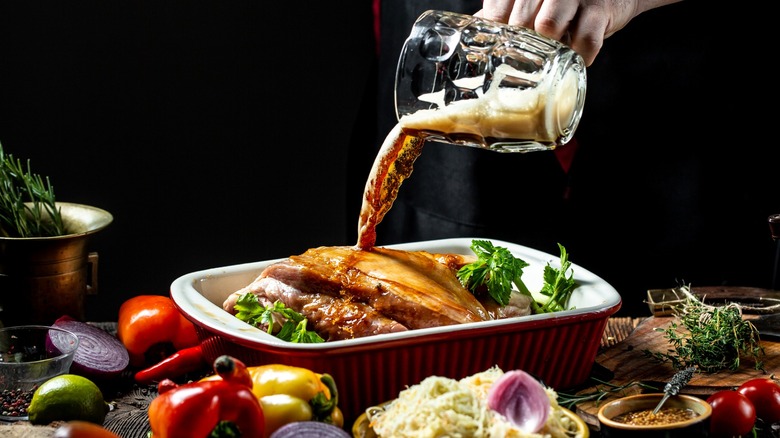 Person pouring glass of beer into meat dish