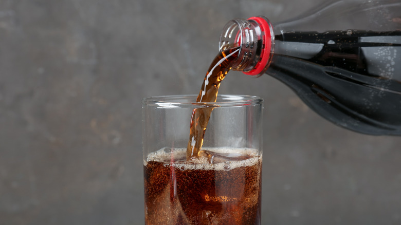Cola being poured from plastic bottle into glass with ice