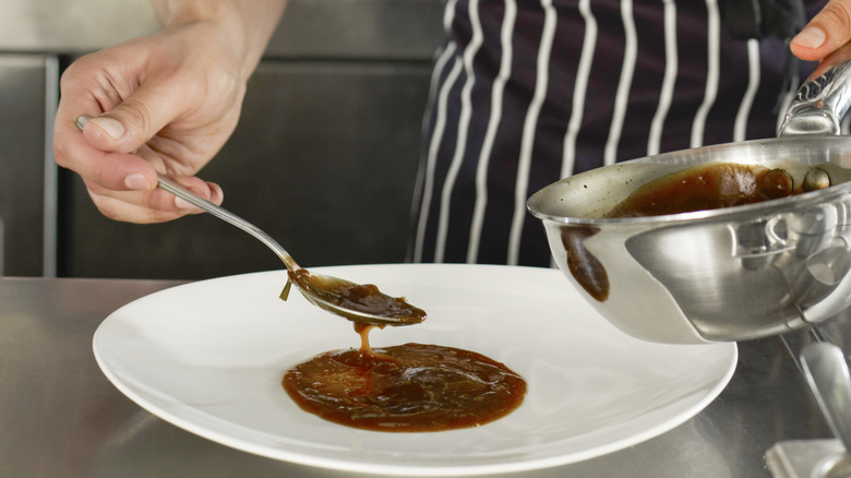 A chef spooning dark brown gravy on a plate.