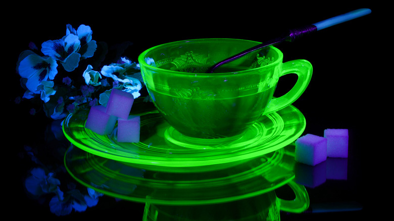 A uranium glass teacup and saucer glow green under a black light