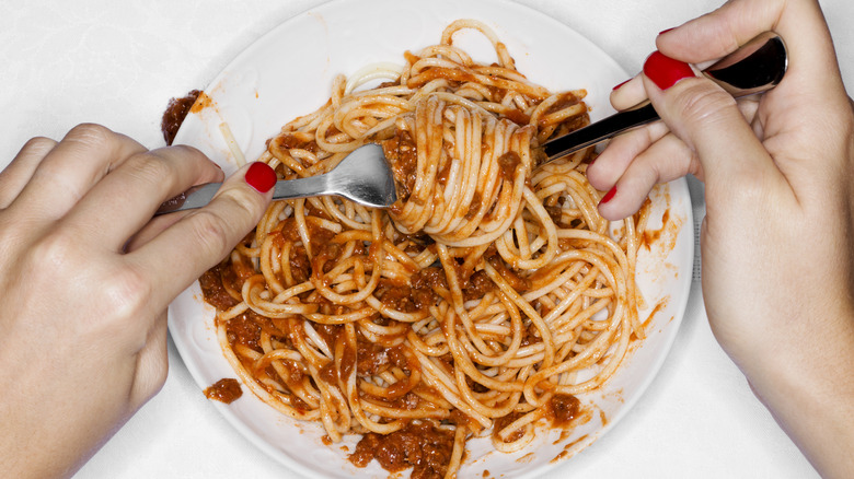 A woman twirls spaghetti with a spoon and fork