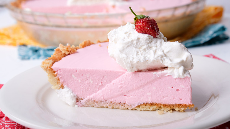 Slice of creamy pink pie with whipped cream and strawberry